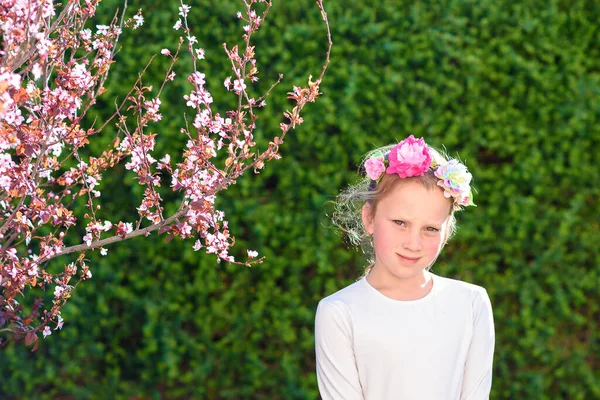 수줍고 아름다운 소녀는 정원에서 카메라를 머리에 화환을 귀여운 아이는 생일을 — 스톡 사진