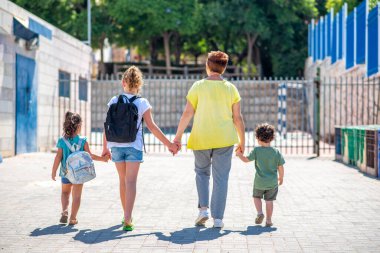 Mutlu okul çocukları büyükanneleriyle okula gidiyor. Öğrenciler ve sırt çantalı büyükanneler anaokuluna gidiyor..