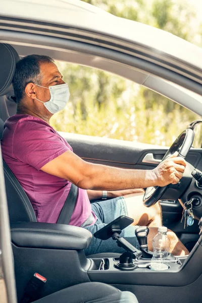 Senior man in protective sterile medical mask driving car. The concept of preventing the spread of the coronavirus.