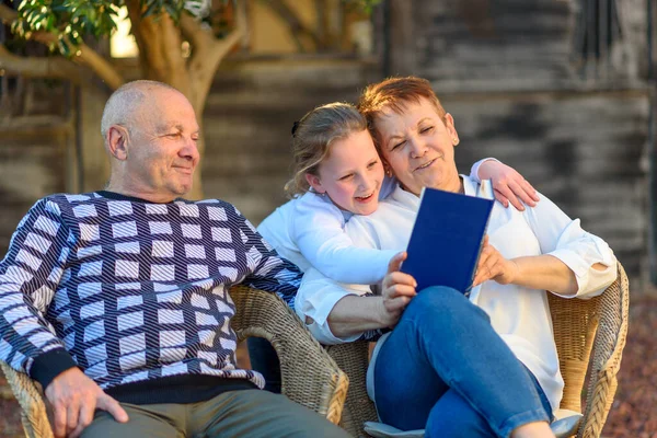 Schöne glückliche Großmutter und Großvater lesen Enkelin Buch in der Natur bei Sonnenuntergang. — Stockfoto