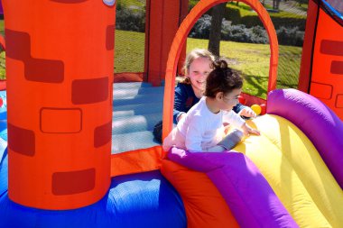 Güneşli bir yaz gününde şişme şato. İki küçük mutlu kız şişme bir şatoda kaydırağın üzerinden atlayıp oynuyorlar..