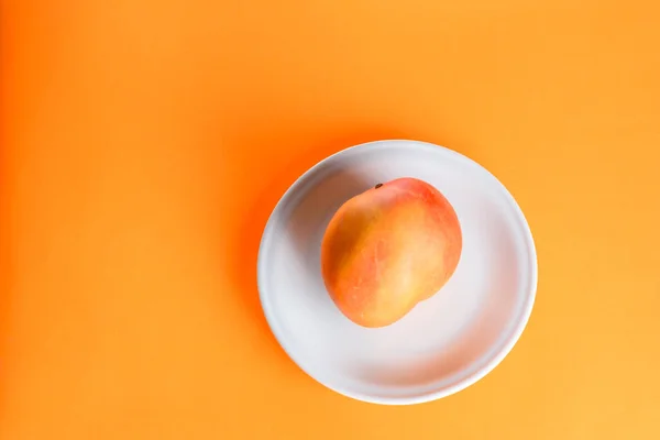 Čerstvé mango tropické ovoce na talíři na oranžovém pozadí. — Stock fotografie