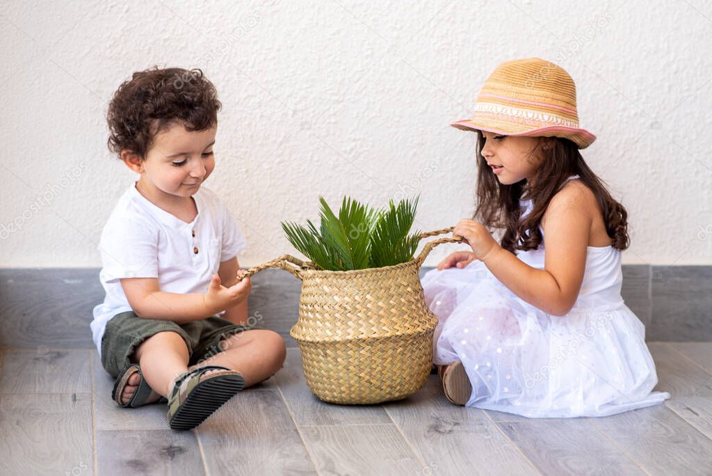 Two young children playing together holding a plant in a trendy straw basket.