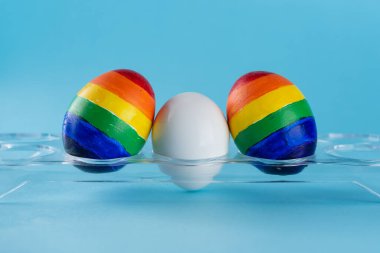 Lgbt ailesi. LGBT bayrağı renginde yumurta ve mavi arka planda beyaz yumurta. Taşıyıcı annelik yasası için yaratıcı fikir, değil mi homoseksüel çift evlat edinme ve çocuk yetiştirme