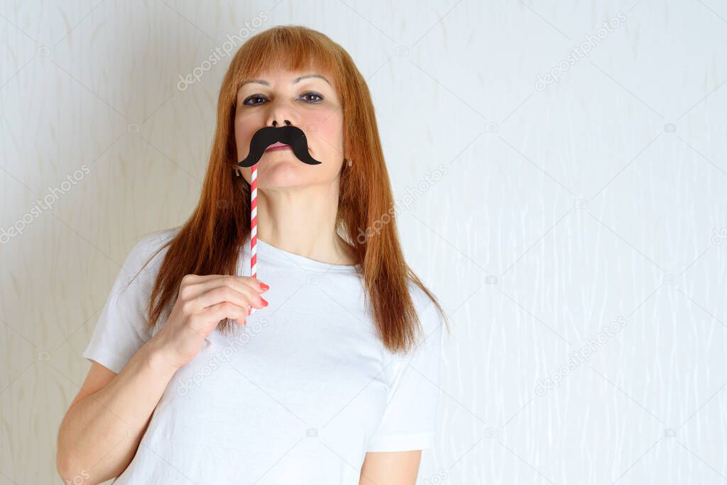 Attractive happy middle aged woman having fun with a fake moustache on stick. Senior female in period menopause. Lifestyle, Women's Health concept : playful mature ready for party. Impostor syndrome.