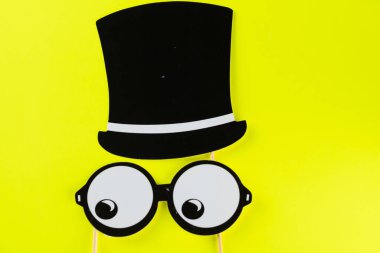 Sarı arka planda komik maske gözlüğü ve şapkanın üst görüntüsü. Parti, doğum günü, Cadılar Bayramı Babalar Günü, Purim, Aptal Günü konsepti.
