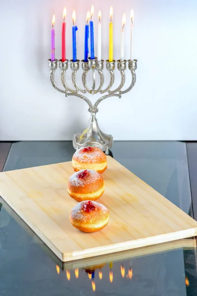 Chanoeka viering concept. Close up zicht op smakelijke donuts met jam en menorah traditionele kandelaar. — Stockfoto