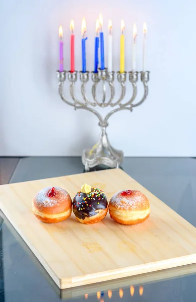 Chanoeka viering concept. Close up zicht op smakelijke donuts met jam en menorah traditionele kandelaar. — Stockfoto