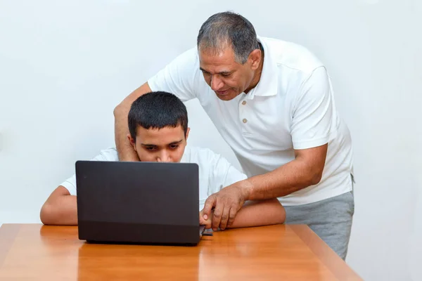 Senior Father and teenage son using laptop. Boy and dad sitting at home working with tablet computer.