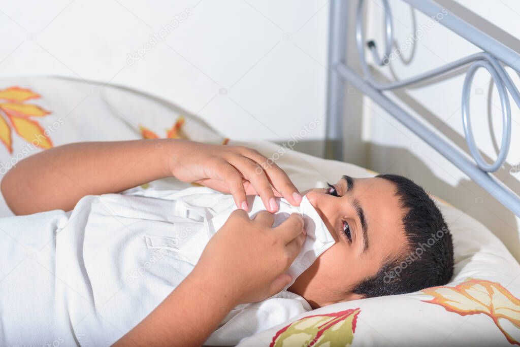 Brunette Teenager Boy Lying On Bed Blowing His Nose.