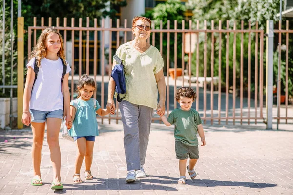 Großmutter und Schüler händchenhaltend mit Schulranzen zur Schule, zu Fuß zum Schulbus. — Stockfoto