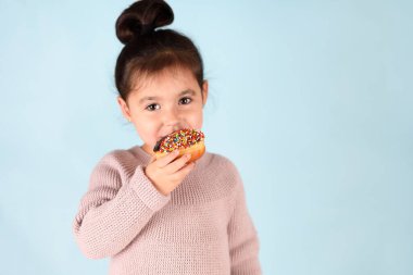 Mavi arka planda donut yiyen küçük mutlu kız..