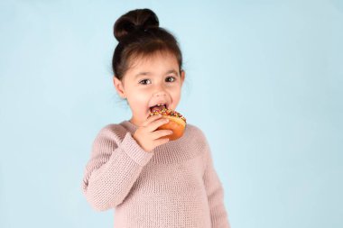 Mavi arka planda donut yiyen küçük mutlu kız..