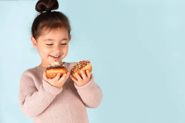 Mavi arka planda donut tutan küçük mutlu kız..