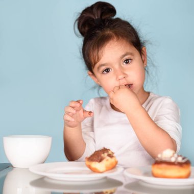 Mavi arka planda donut yiyen küçük mutlu kız..
