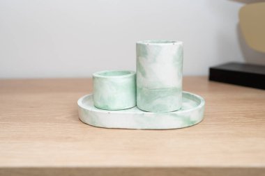 Değişen yüksekliklerde üç zarif mermer mum tutacağı dairesel bir tepsiye konur. Yumuşak yeşil ve beyaz renkler, açık ahşap yüzeyle çok güzel tezat oluşturuyor..