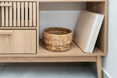 Şık ahşap depolama ünitesinde örülmüş bir sepet ve sergilenmekte olan kitaplar yer alıyor. Minimalist tasarım, odanın çağdaş iç yapısını geliştirir..