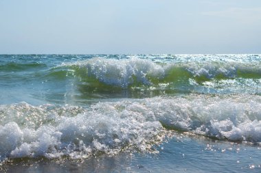 Deniz dalgaları kıyıya vurdu. Köpüklü dalga yaklaşıyor. Sahildeki masmavi su..