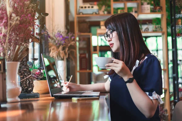 Business Asian woman hold cup of coffee working with laptop computer on in coffee shop like the background.