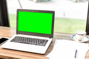 Boş Yeşil ekranlı dizüstü bilgisayarın mockup görüntüsü, akıllı telefon, kahve dükkanının ahşap masasında kahve fincanı.