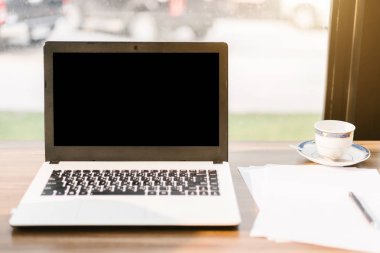 Kahve dükkanı ahşap masada boş siyah ekran, akıllı telefon ve belge ile dizüstü mockup görüntü.