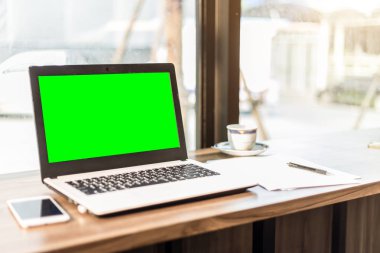 Boş Yeşil ekranlı dizüstü bilgisayarın mockup görüntüsü, akıllı telefon, kahve dükkanının ahşap masasında kahve fincanı.