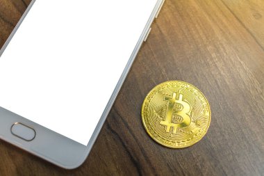 Bitcoin sikke ve akıllı telefon üstünde eski ahşap masa üzerinde.