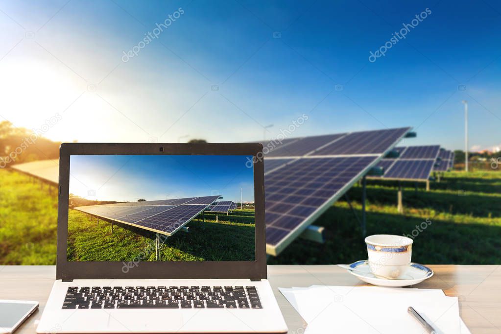 Mockup image of laptop with solar panel screen,smartphone,coffee cup on wooden table blurred images of solar panel on blue sky background, Alternative energy concept,Clean energy,Green energy.