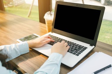 Boş siyah ekran ile dizüstü bilgisayar ile çalışan iş kadın yakın çekim bir not belgesi ve arka plan gibi kahve dükkanında akıllı telefon yapmak.