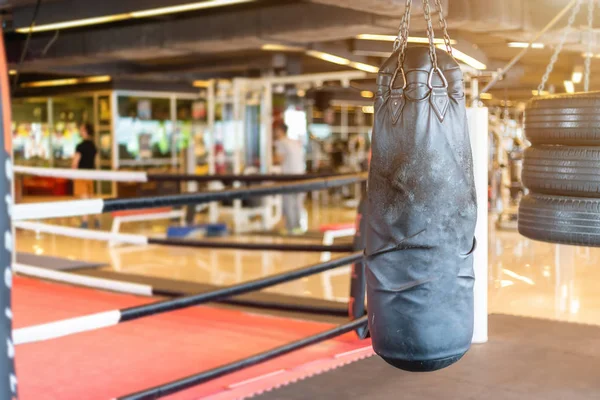 Black punching bag hanging in Abstract blur of defocused boxing gym interior and fitness health club with sports exercise equipment Gym blur background.