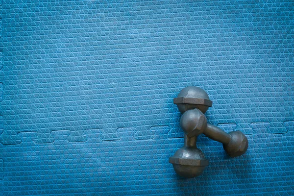 Halteres em um piso de borracha azul vazio no esporte desfocado — Fotografia de Stock