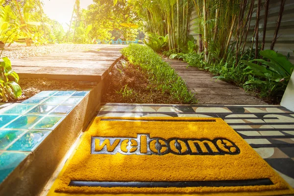Welcome doormat on green grass lawn in fresh summer garden background,with warm sunset sunlight.