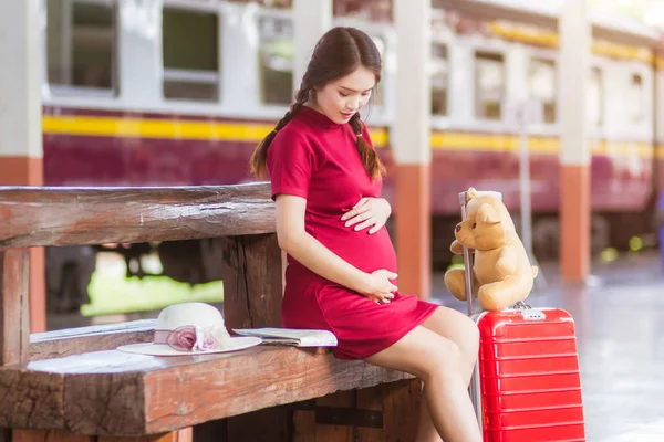 アジアの女性妊娠中の赤いドレスは、再運びでベンチに座って — ストック写真