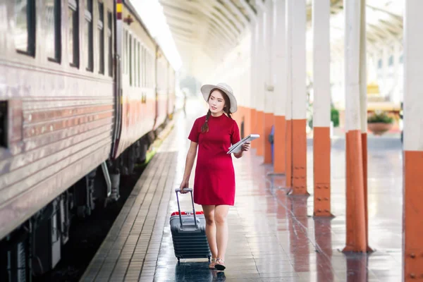 Mujer asiática embarazada de vestido rojo de viaje con maleta roja en ra —  Fotos de Stock