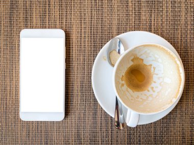 Üst görünümde ahşap masada Akıllı telefon ve Boş kahve fincanı. 