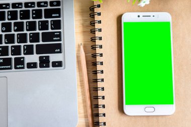 Not defterinde akıllı telefon, kalem ve saksı ağacı olan bir dizüstü bilgisayar. 