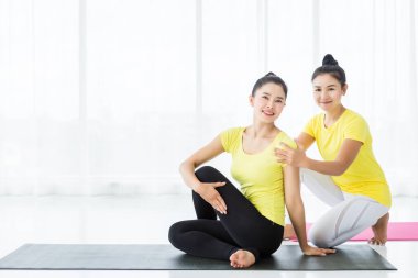 Sarı elbiseyle yoga yapan iki genç Asyalı kadın.