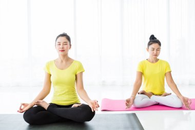 Sarı elbiseyle yoga yapan iki genç Asyalı kadın.