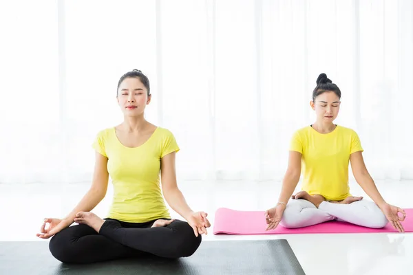 Two young Asian women workout practicing yoga in yellow dress or