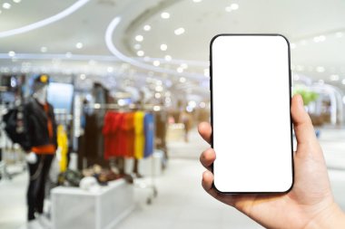 Kadın kullanımına yakın plan: Boş beyaz ekran ile el kameralı akıllı telefon, alışveriş merkezinin arka planındaki soyut bulanık görüntüler, online alışveriş kavramı.