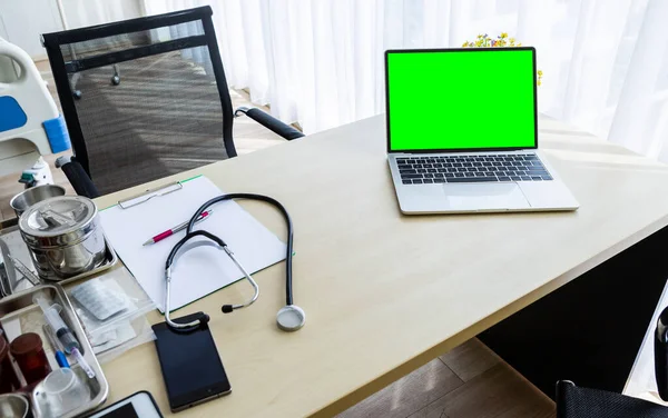 laptop computer with a blank green screen with stethoscope,vial,syringe,empty paper clipboard and medical bottle different drugs on surgical tray with medical equipment on wooden table background