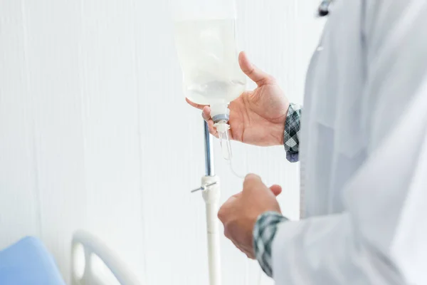 Genç doktor terapi uzmanının yakın plan fotoğrafı. Steteskopla gülümseyen bir yüz. Hastane geçmişinde salin şişesi var..