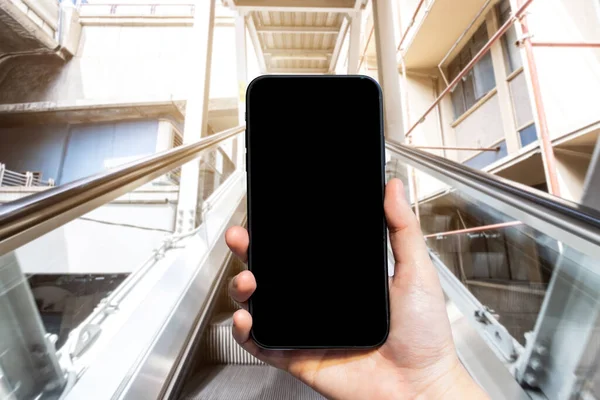 Close-up of female use Hand holding smartphone with empty blank white screen blurred images touch of Abstract blur of mechanical escalator for people going up and down, modern escalators in mall