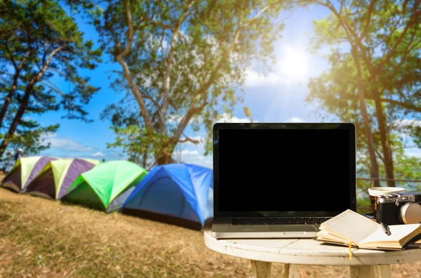 Mockup of laptop computer with empty screen with camera,notebook,coffee cup on table at in forest summer camp among meadow on Mountain,recreation and Tourist holiday outdoor concept
