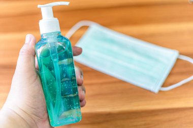 Mavi alkollü el dezenfektanı soyut tek kullanımlık tıbbi maskenin soyut bulanıklığı ev arka plandaki odada COVID-19 virüs enfeksiyonunun yayılmasını önleme kavramı.