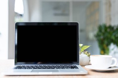 Kahve dükkanının arka planında kahve fincanı olan boş ekranlı dizüstü bilgisayarın modeli, siyah ekran.