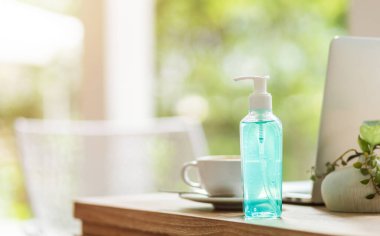 Kahve dükkanının masasında dizüstü bilgisayarı ve kahve fincanı olan alkollü el dezenfektanı ofis arka planı, COVID-19 virüs enfeksiyonu.