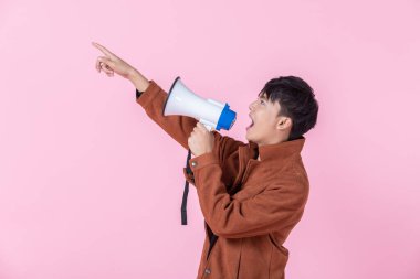 Asyalı genç, yakışıklı, bağıran bir adam. Yan gözlerinde megafonla aşkla kameraya bakıyor. Pembe boş fotokopi stüdyosu arka planında izole edilmiş..