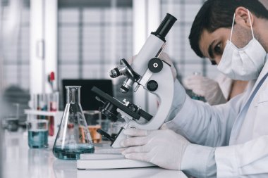 Kimya laboratuarındaki bir bilim adamının araştırmacısı Microscope 'a örnek test tüpüyle bakan erkek bilim adamı laboratuvar analizinde araştırma yapıyor.