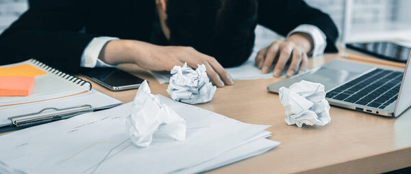 Stressed businessman worked with laptop computer and having a headache after business losses abstract blur with focus crumpled sheet of paper In the office room background.